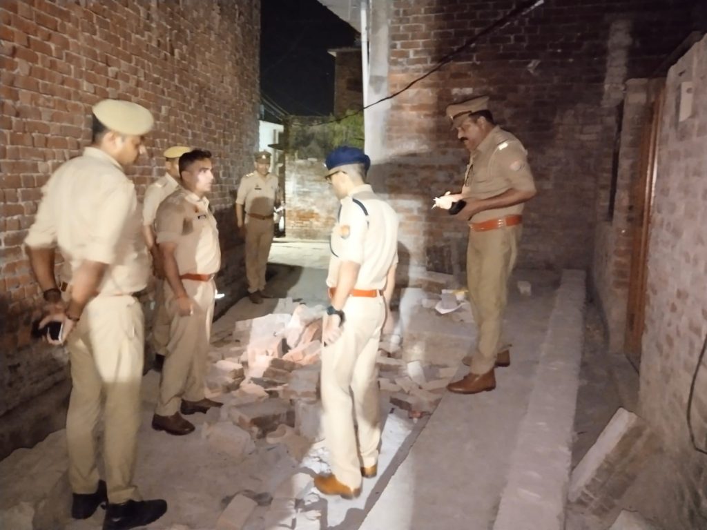 Group of police officers in khaki uniforms standing in a narrow brick alley, inspecting scattered bricks.