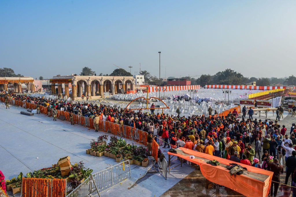 Large outdoor festival with orange drapes, archways, and crowds seated along barriers.