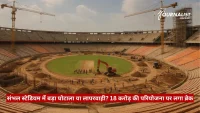 A large stadium under construction with two tall cranes and workers on the field.