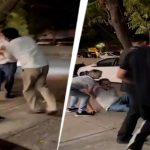 Group of men restraining a man during a nighttime street altercation, with onlookers and a white car in the background.
