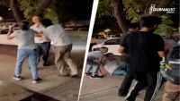 Group of men restraining a man during a nighttime street altercation, with onlookers and a white car in the background.
