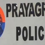 Signboard reading 'PRAYAGRAJ POLICE' with a crest emblem on the left and a watermark in the corner (informational image).