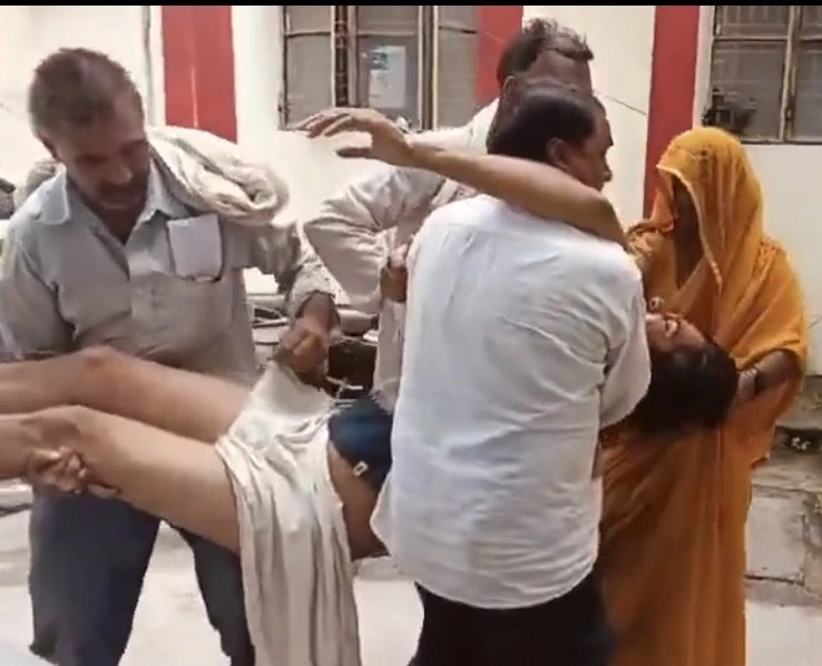 GxFpK0ZXkAAY_4H - The Journalist News Group of adults lifting a man horizontally while others assist nearby; a woman in an orange sari watches nearby.
