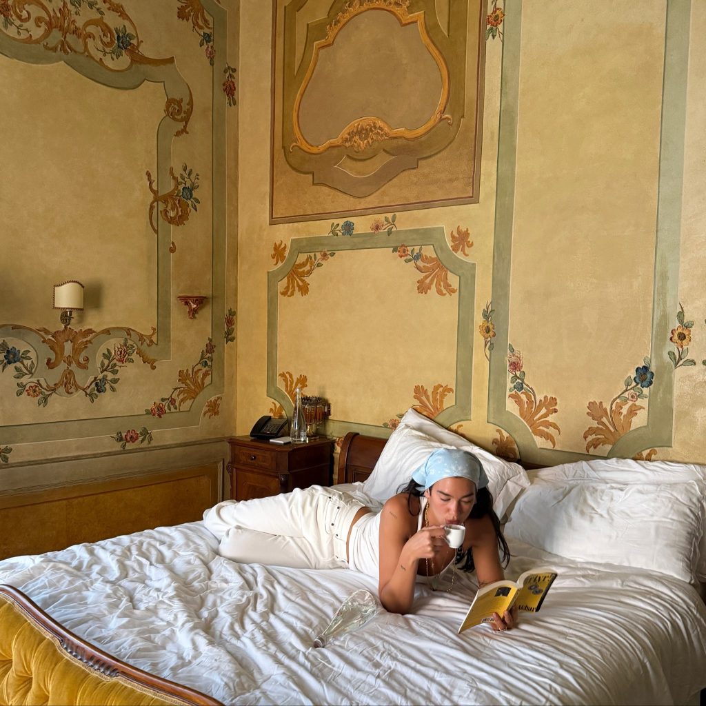 Two people relaxing in a lavishly decorated hotel room bed, reading magazines together.