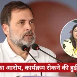 Man with a gray beard speaking into two microphones at a press conference; circular inset shows a woman speaking at a panel, with a red Hindi caption banner across the bottom.
