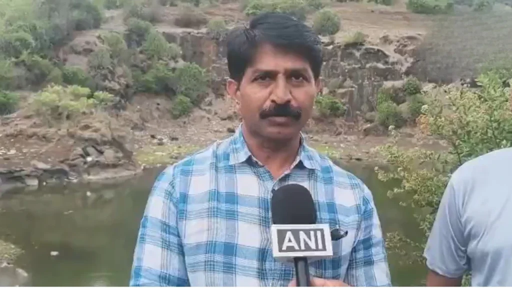 Man in a blue plaid shirt being interviewed outdoors, holding a mic labeled 'ANI' near a river and rocky hillside.