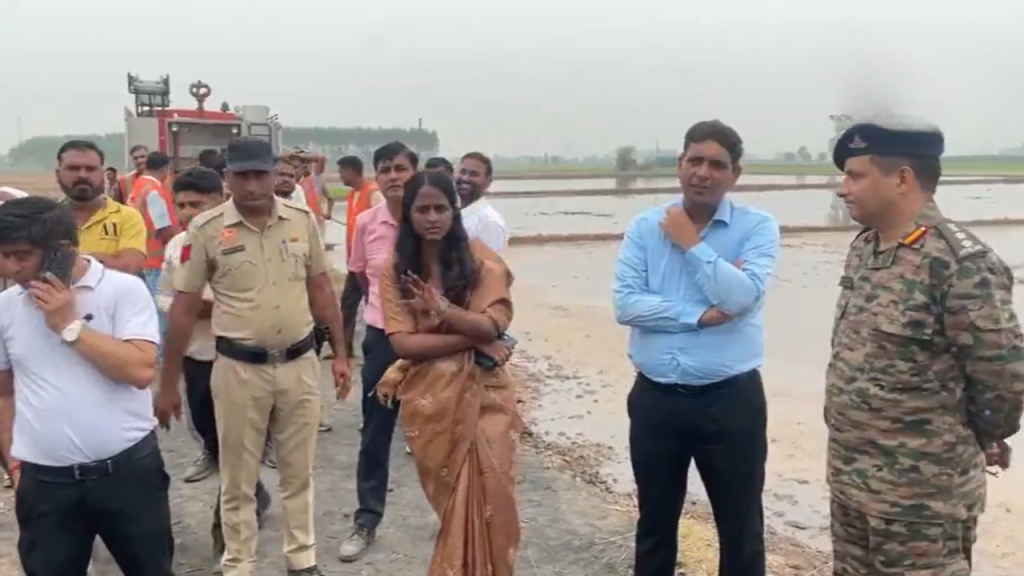 Group of uniformed officers and civilians standing on a muddy, flooded field, discussing at a site inspection.