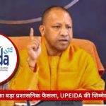 Official in orange robes speaks at a press conference; raised index finger, UPEIDA logo prominent, with a red Hindi banner about changes to UPEIDA responsibilities.