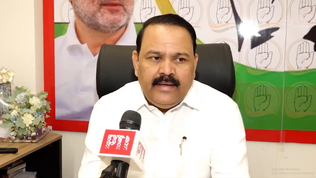 Man in a white shirt speaking into a PTI microphone during a press interview, with a political backdrop behind him.