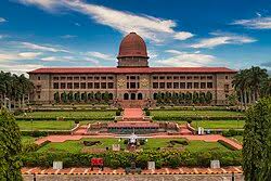 Red-brick domed building with formal gardens and steps, under a blue sky, front view