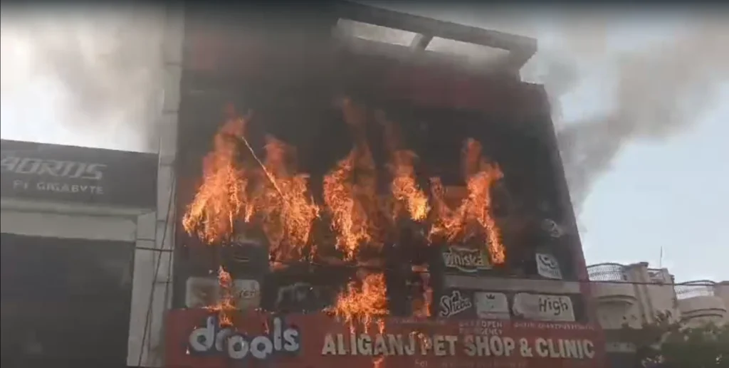 Screenshot 2026-06-22 173454 - The Journalist News Two-story storefront building on fire with large flames and thick smoke rising from the entrance area outdoors, a chaotic street scene nearby.