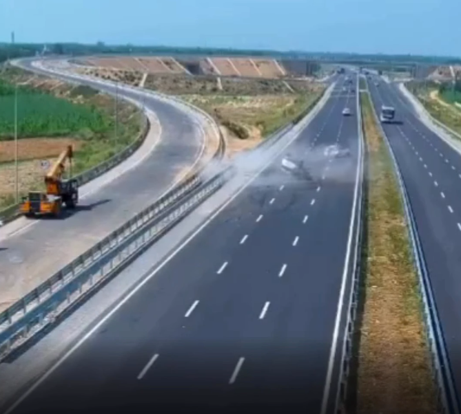 Multi-lane highway under construction with a yellow roadwork vehicle on the left shoulder and freshly paved lanes stretching into the distance.