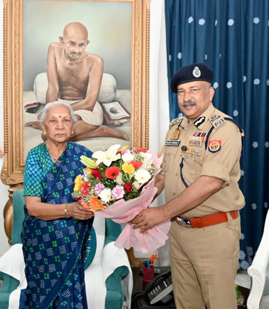 WhatsApp Image 2026-06-02 at 112022 PM - The Journalist News Police officer in uniform presenting a bouquet to an elderly woman in a blue sari, with a large framed portrait of a seated monk behind them.