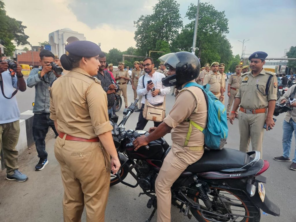 WhatsApp Image 2026-06-02 at 122252 AM - The Journalist News Police officer in khaki uniform talks to a motorcyclist wearing a helmet at a street checkpoint, with reporters and bystanders in the background.