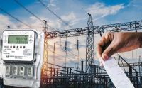 Electric meter in the foreground with a power substation and a hand holding a receipt in the background, suggesting energy billing or usage.