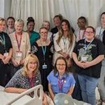 Group of diverse healthcare staff and volunteers posing for a photo in a hospital ward.