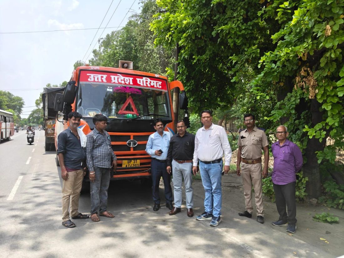 Seven men stand beside an orange transport truck on a sunny road, with lush green trees to the right; the truck has Hindi text on the windshield (likely a transport department name).