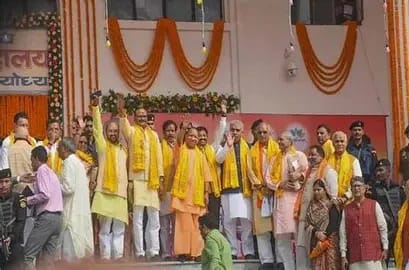 WhatsApp Image 2026-06-03 at 114912 PM - The Journalist News Group of people on a stage at a ceremonial event, many wearing yellow scarves, with orange and floral decorations in the background.