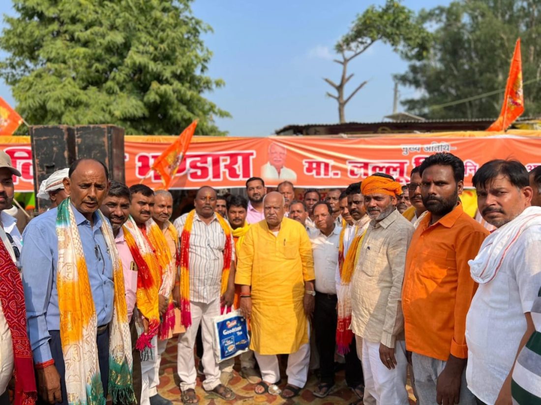 Group of Indian men in traditional attire posing at a political rally, orange banners in the background.