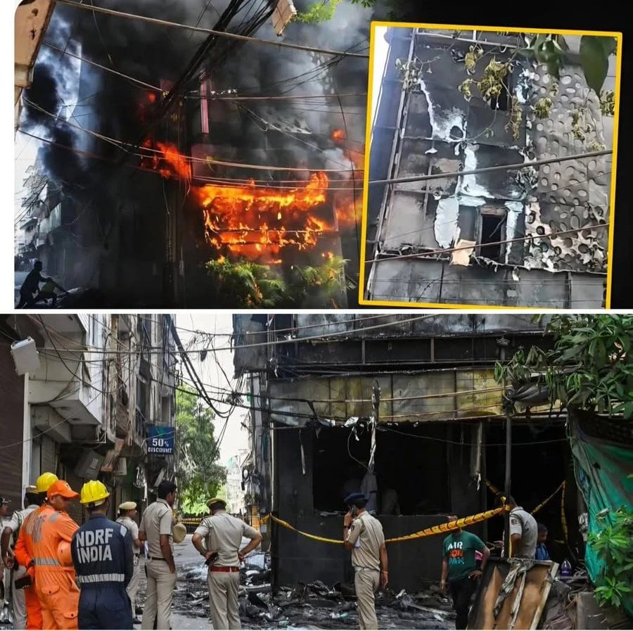 Fire responders, including NDRF, stand near a burned, smoke-filled building as onlookers and debris line the street after a large fire broke out in a narrow urban alley. An inset shows a damaged facade with scorched walls and exposed interior.