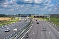 Multi-lane highway with cars and a motorcycle traveling under an overpass on a sunny day.