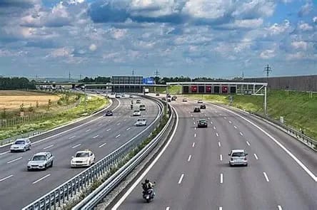 Multi-lane highway with cars and a motorcycle traveling under an overpass on a sunny day.