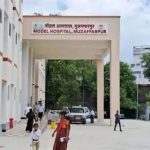 Entrance to Model Hospital, Muzaffarpur: a white archway with a sign, people walking in a paved courtyard.