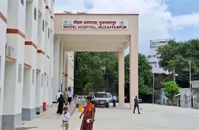 Entrance to Model Hospital, Muzaffarpur: a white archway with a sign, people walking in a paved courtyard.