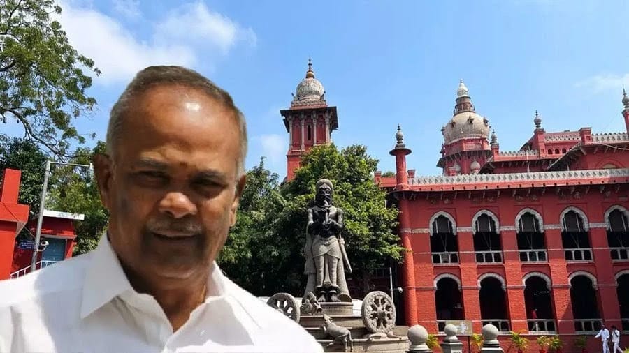 Man in a white shirt smiles in the foreground with a red historic building, statue, and domed towers in the background.