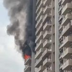Fire on a balcony of a tall apartment building with thick black smoke rising from the upper floor.