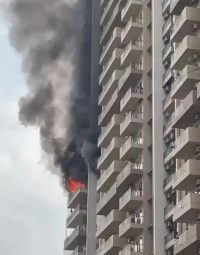 Fire on a balcony of a tall apartment building with thick black smoke rising from the upper floor.