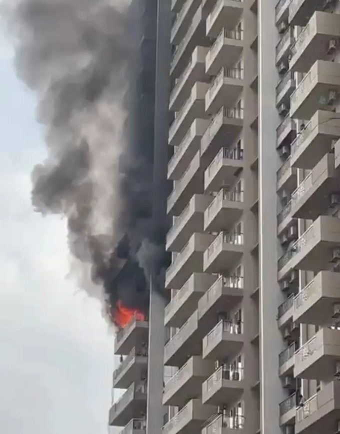 Fire on a balcony of a tall apartment building with thick black smoke rising from the upper floor.