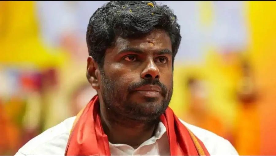 Close-up of a man wearing a white shirt and red ceremonial scarf, looking to the side at a festive event.