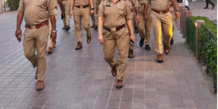 Group of police officers in khaki uniforms walking down a paved sidewalk together in an urban setting.