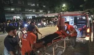 WhatsApp Image 2026-06-08 at 21316 PM - The Journalist News Nighttime emergency scene: paramedics in red uniforms transport a patient on a stretcher toward an ambulance, with onlookers nearby under tents and lights.