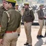 Group of uniformed officers standing in formation on a parade ground, some holding rifles, wearing yellow caps and brown belts.