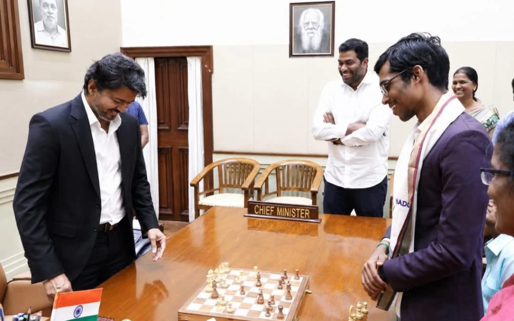 WhatsApp Image 2026-06-08 at 44037 PM - The Journalist News Two men play chess at a desk labeled Chief Minister as colleagues smile and watch in a formal office with an Indian flag on the board nearby.