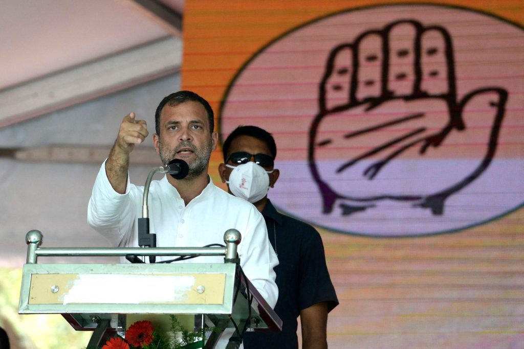 Man at a podium gesturing with a raised finger/fist while speaking, with a large graphic fist behind him on stage backdrop.