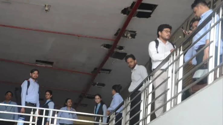 images 13 - The Journalist News Group of men in light blue shirts with backpacks standing on a staircase landing along a metal railing in an indoor corridor.