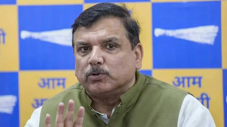 Man with a mustache in a green vest over a white shirt speaks at a press conference, gesturing with his hand in front of a blue-yellow backdrop with a political party logo.