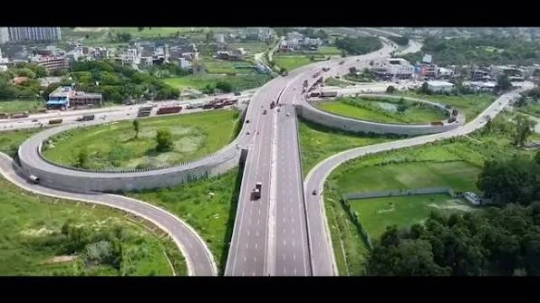 images 2 - The Journalist News Aerial view of a cloverleaf highway interchange with a central elevated road, looping ramps, and surrounding greenery; several vehicles travel on the lanes.