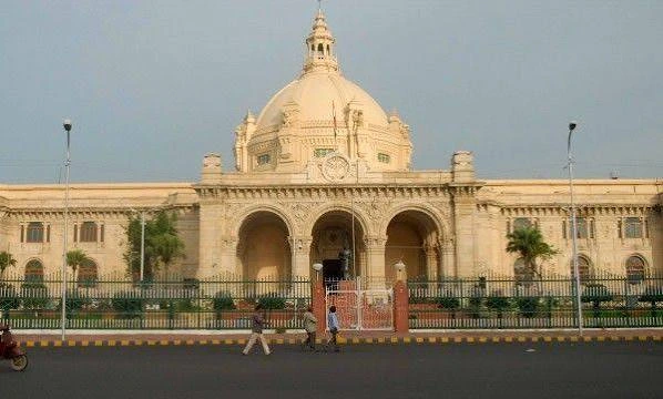 images 3 - The Journalist News Grand beige domed building with three arched entrances, palm trees, and a fence in front; a street with pedestrians and a motorbike passes by.