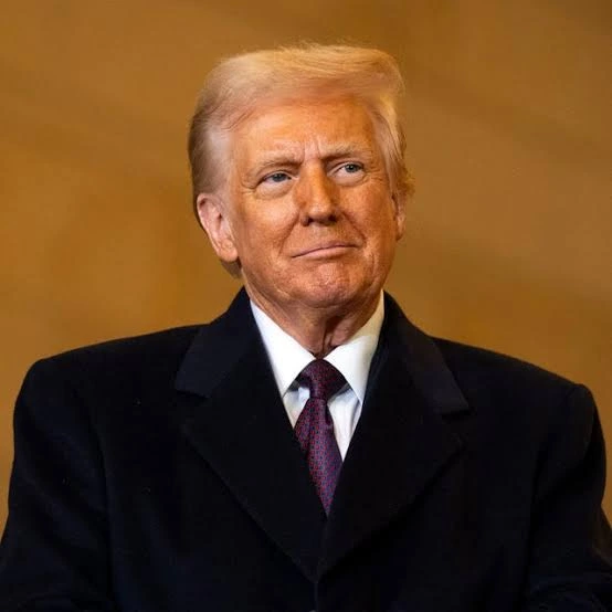 Portrait of a mature man with light hair in a dark suit and maroon tie, looking to the right against a brown background.