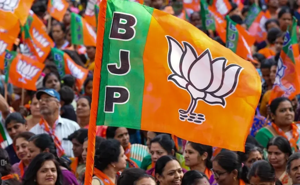rvhbrvnvsguii2vwhkkp - The Journalist News Flag of the BJP with its orange and green design and lotus symbol in a crowded political rally background.