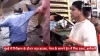 Split-screen news clip: on the left, a man in a blue shirt appears to stumble or fall near rubble; on the right, a female reporter holds a microphone at a street-side news setup, with a Hindi caption bar mentioning a BMC employee incident.