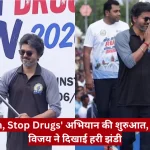 Man in sunglasses and a two-tone polo leads a drug-awareness run as a large crowd watches; a red Hindi news caption bars the bottom of the image.