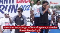 Man in sunglasses and a two-tone polo leads a drug-awareness run as a large crowd watches; a red Hindi news caption bars the bottom of the image.