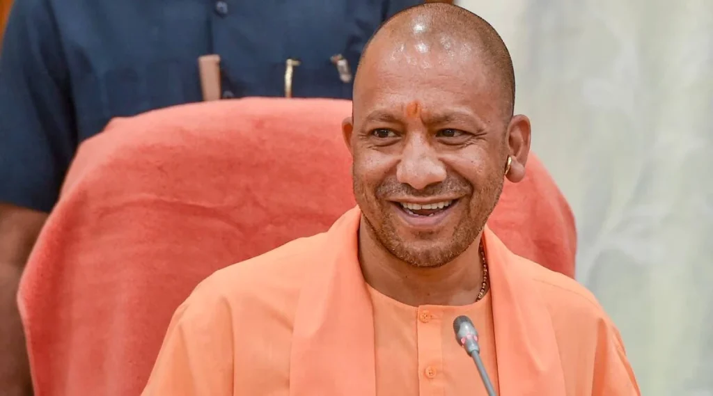 Smiling man in orange robes speaks at a microphone in a formal setting.