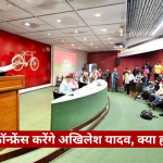 Speaker at a podium delivering a press conference in a studio, with a curved green desk and a crowded audience of reporters and photographers; red wall with bicycle mural and The Journalist logo in the corner.