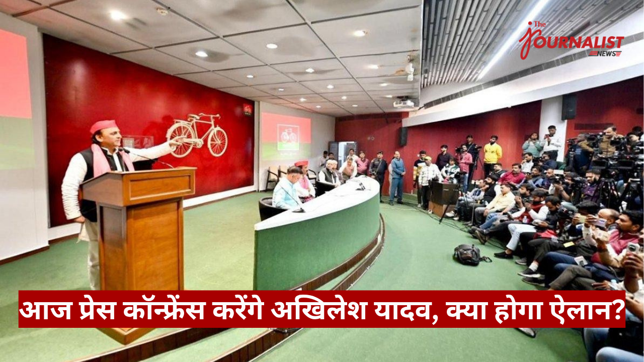 Speaker at a podium delivering a press conference in a studio, with a curved green desk and a crowded audience of reporters and photographers; red wall with bicycle mural and The Journalist logo in the corner.